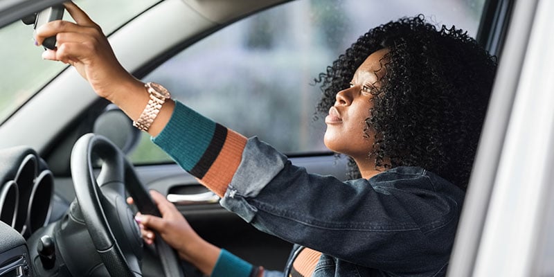 young woman checking her rearview mirrors before beginning to drive